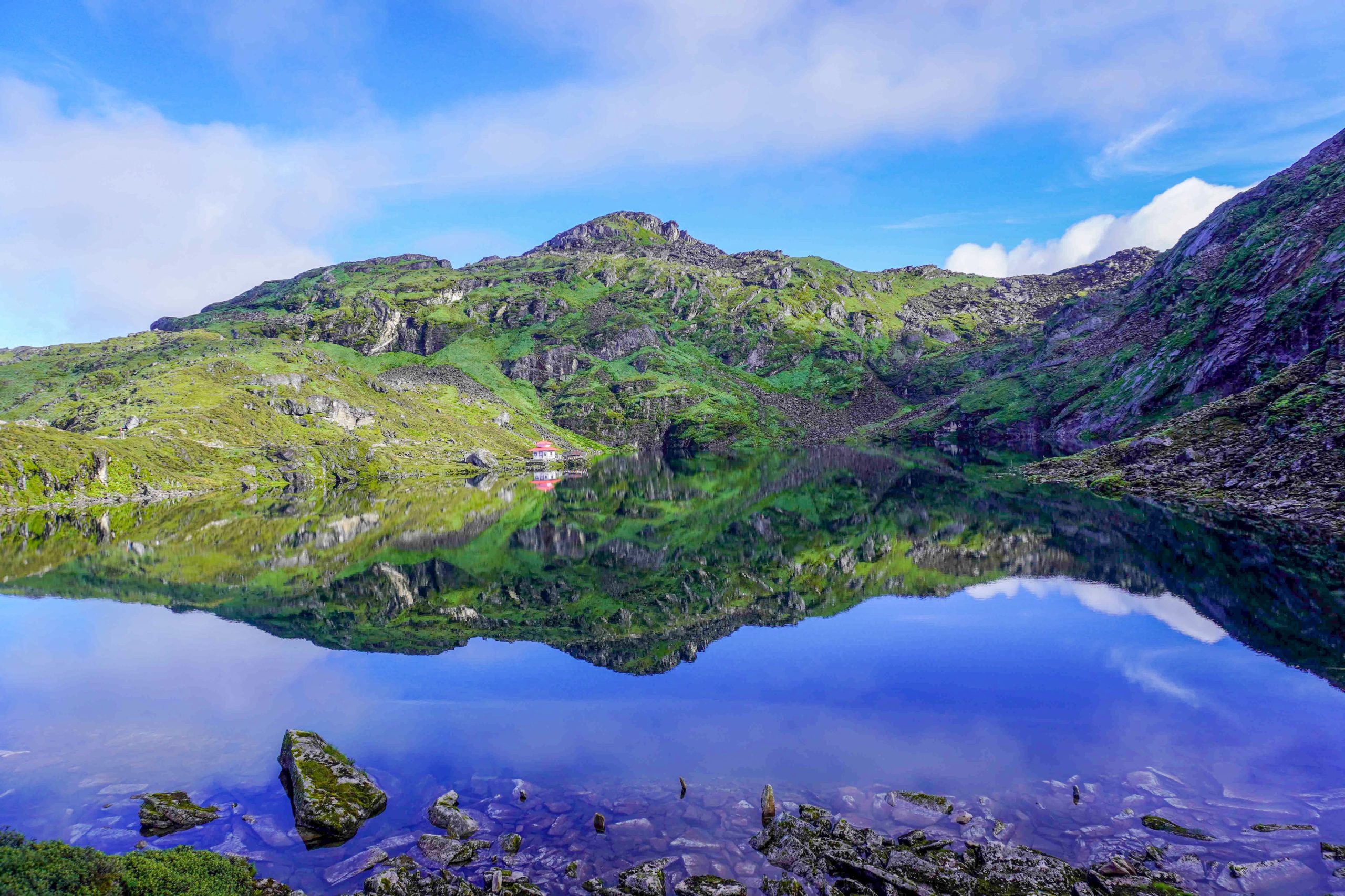 A breathtaking view of a green mountain reflected in a crystal-clear lake under a vibrant blue sky.