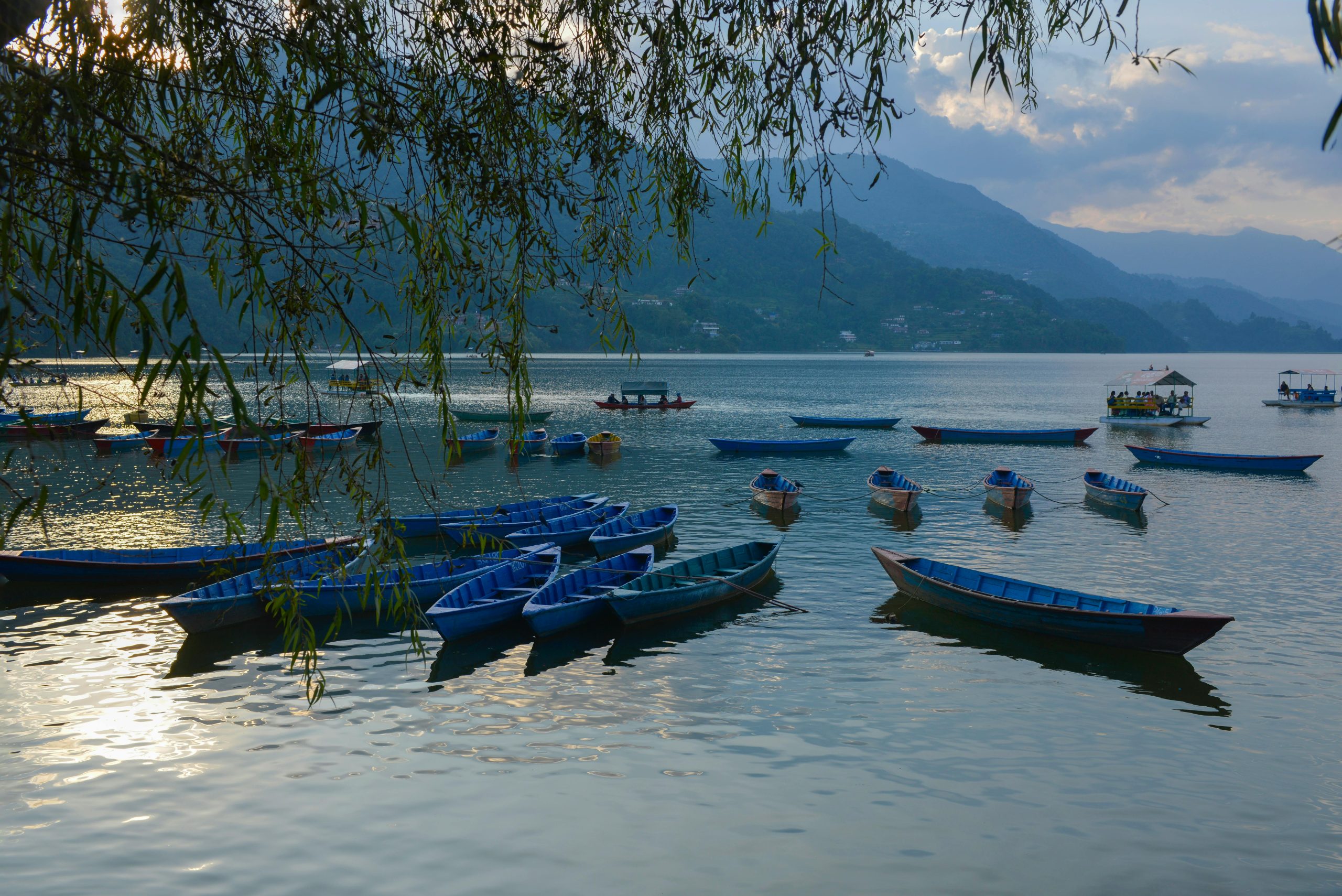 Peaceful scene of blue rowboats on a calm lake at sunset with mountain backdrop.